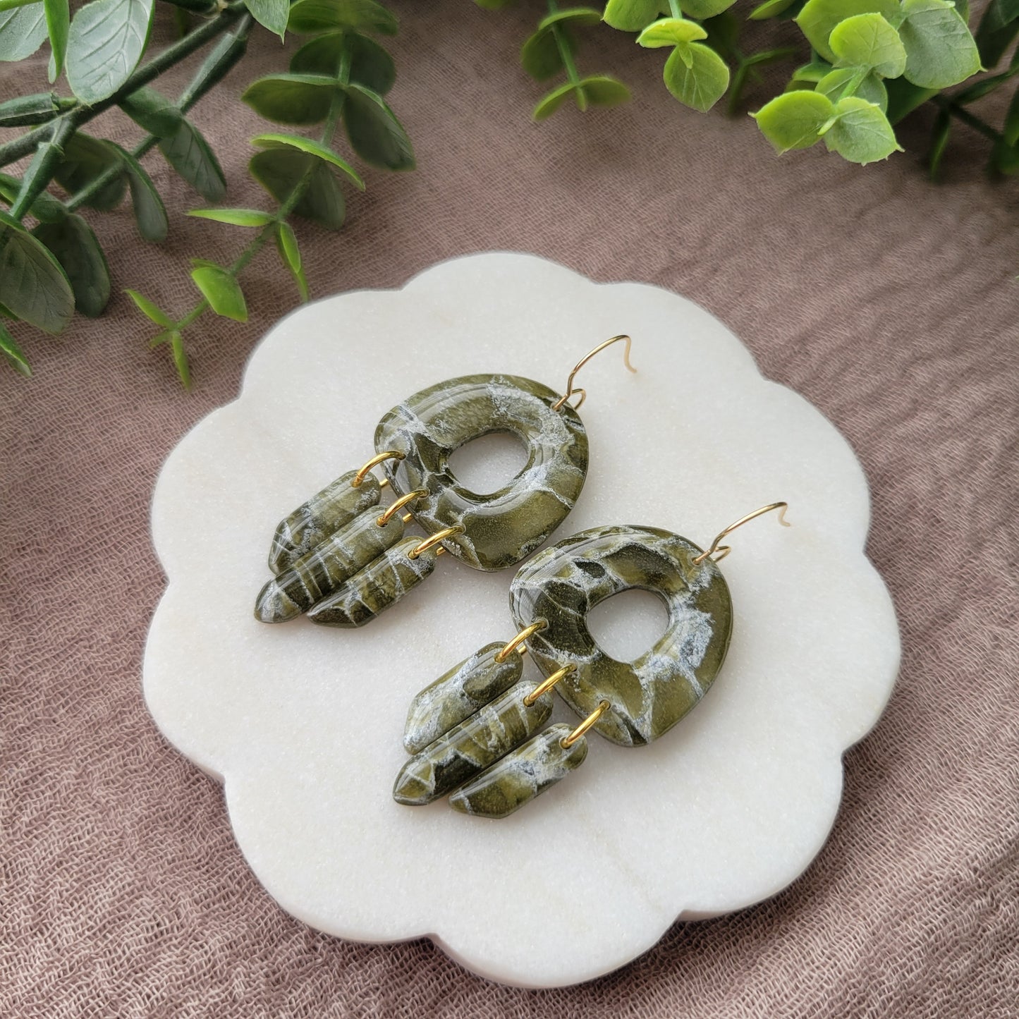 Right side view of a pair of green marble earrings displayed on a white round scalloped tray.