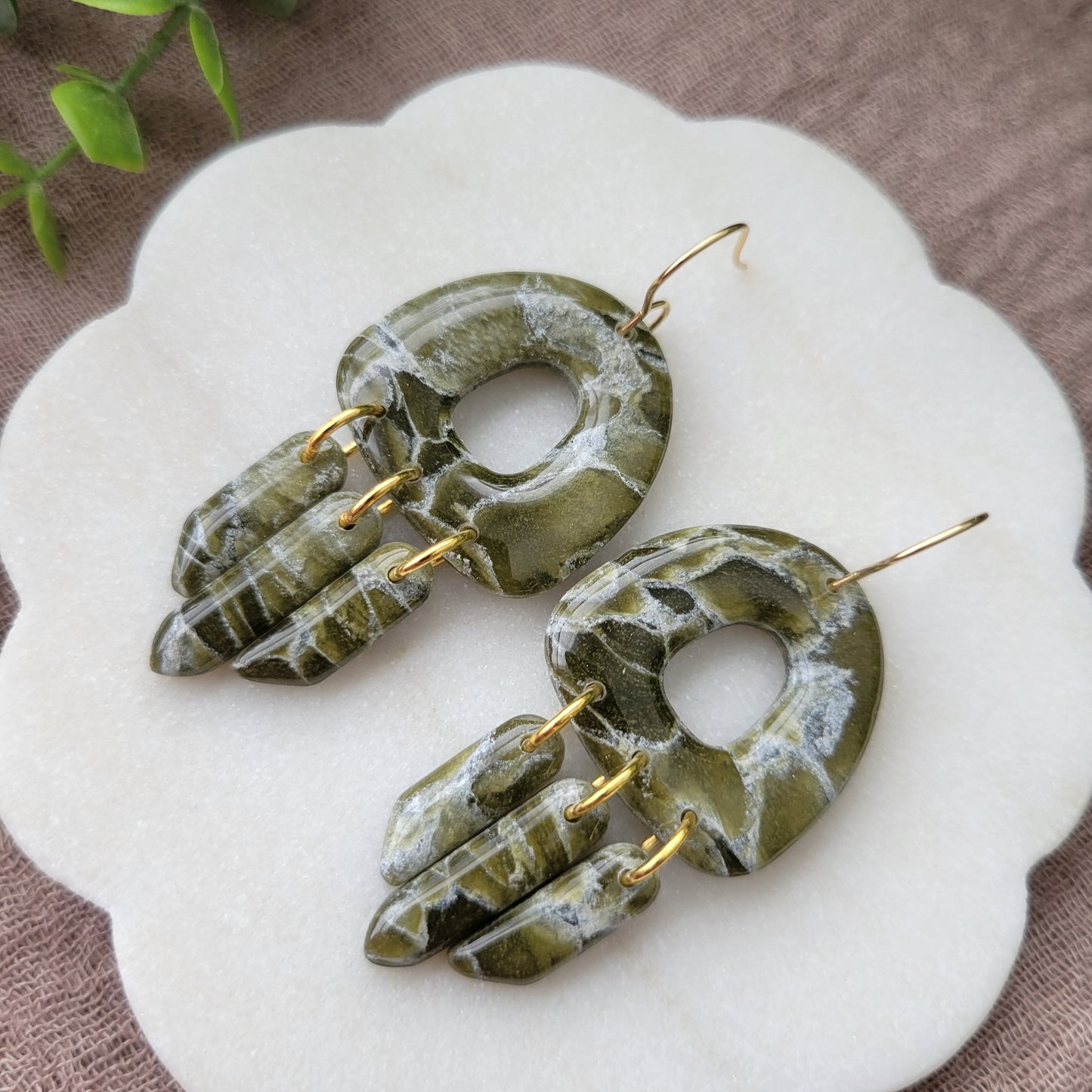 Close up right side view of a pair of green marble earrings displayed on a white round scalloped tray.