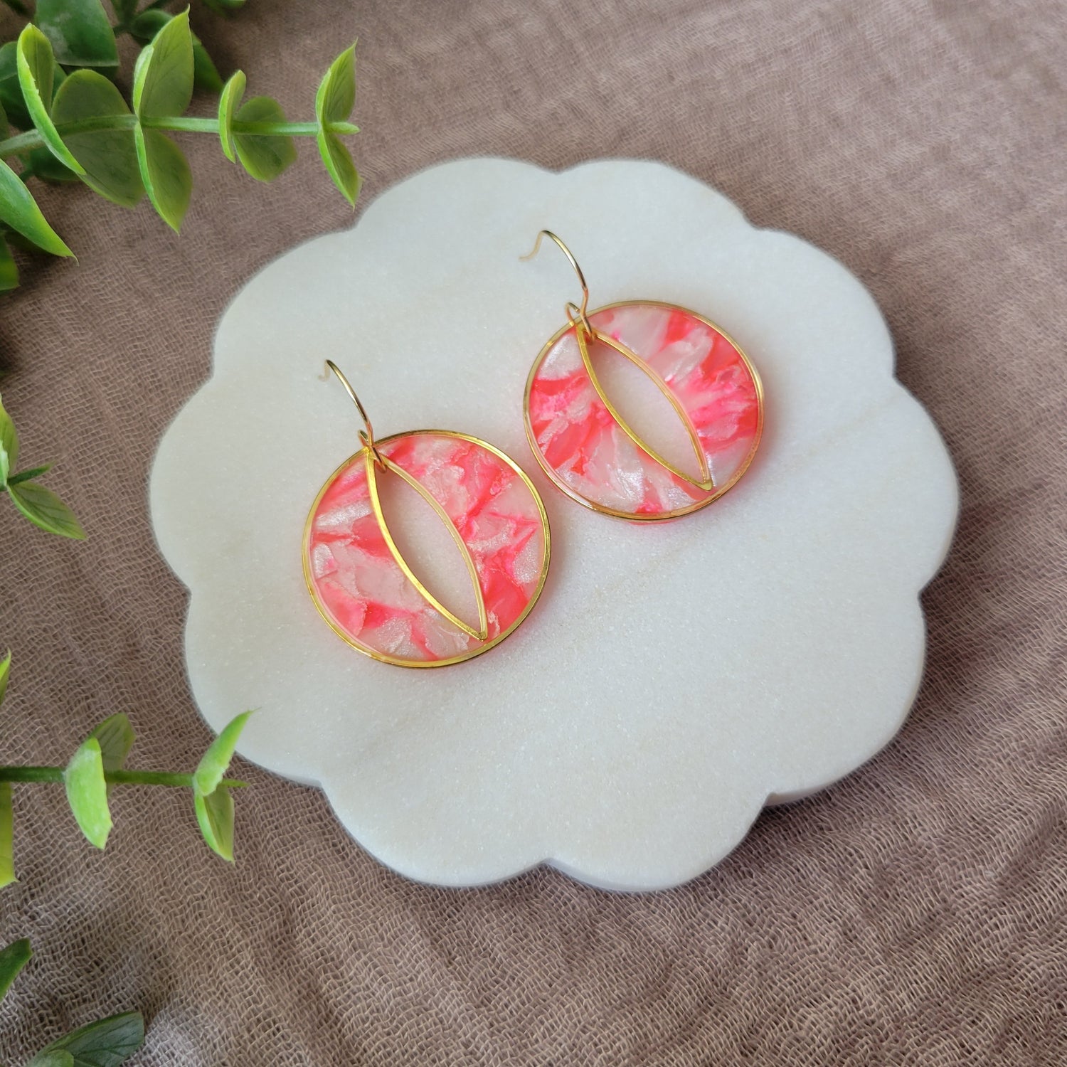 Left side view of a pair of round polymer clay earrings in the color bright pink and pearl with gold trim on a white scalloped tray.