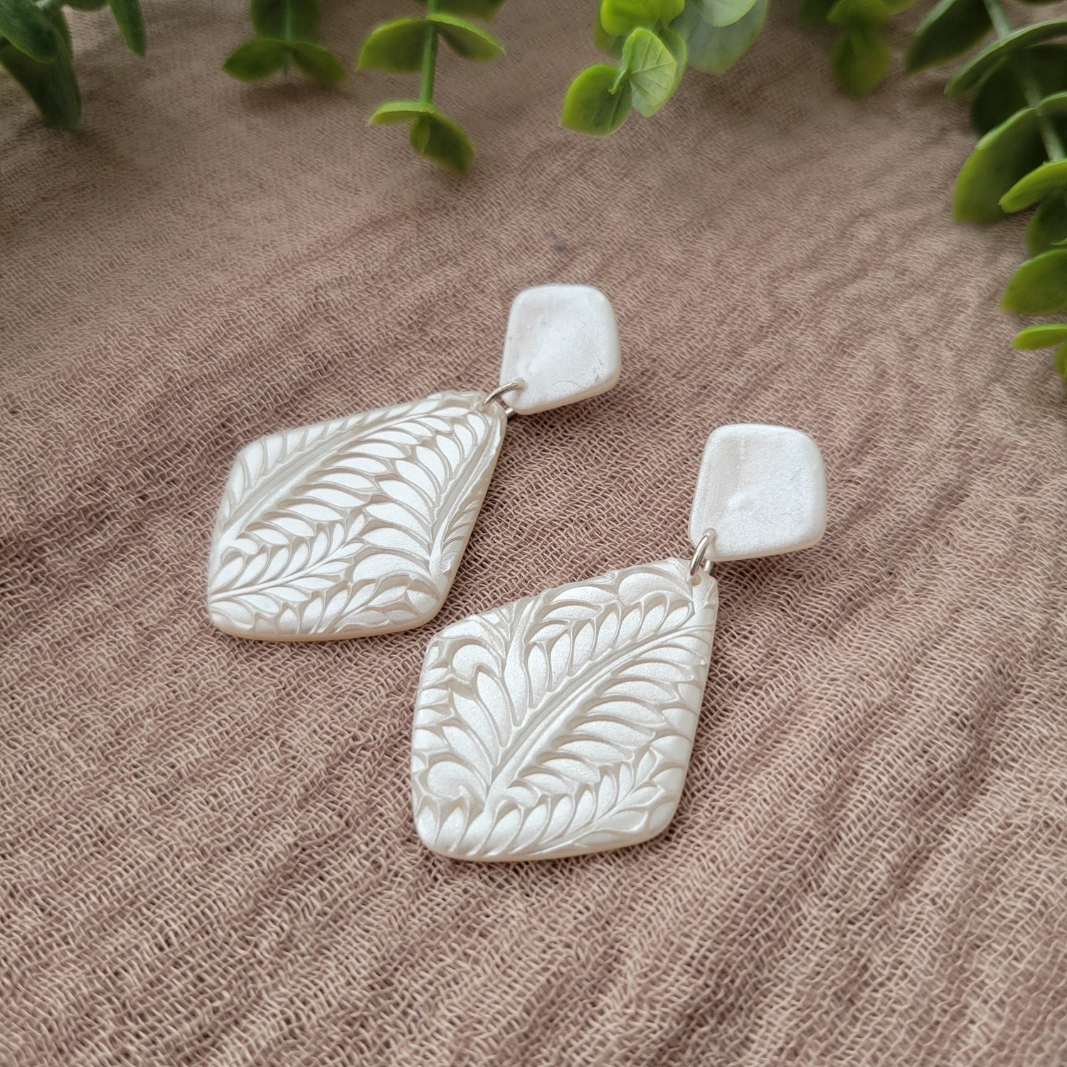 Side view of a pair of earrings with leaf texture in a shimmering pearl color.