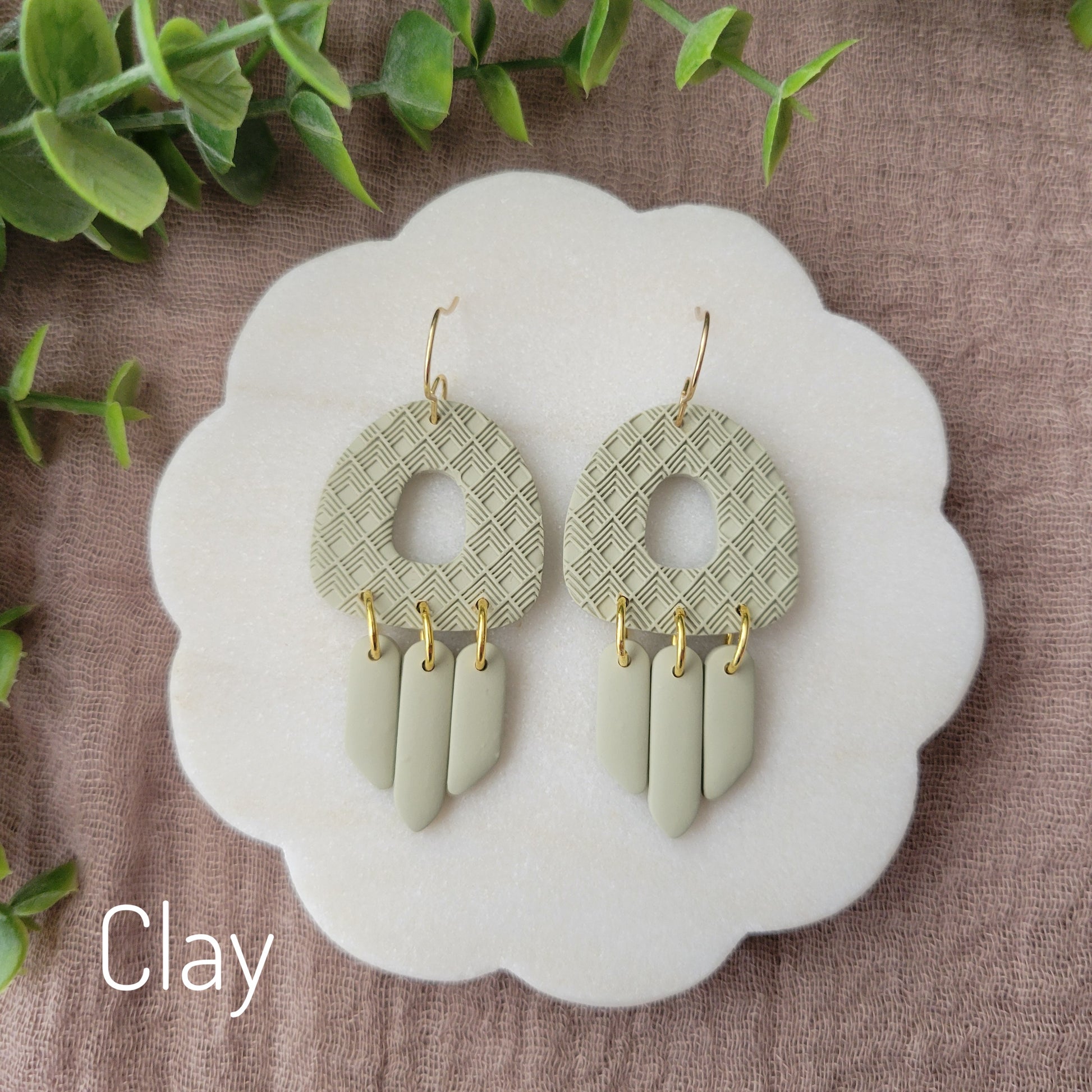 Top view of a pair of green earrings with lattice texture displayed on a white round scalloped tray.