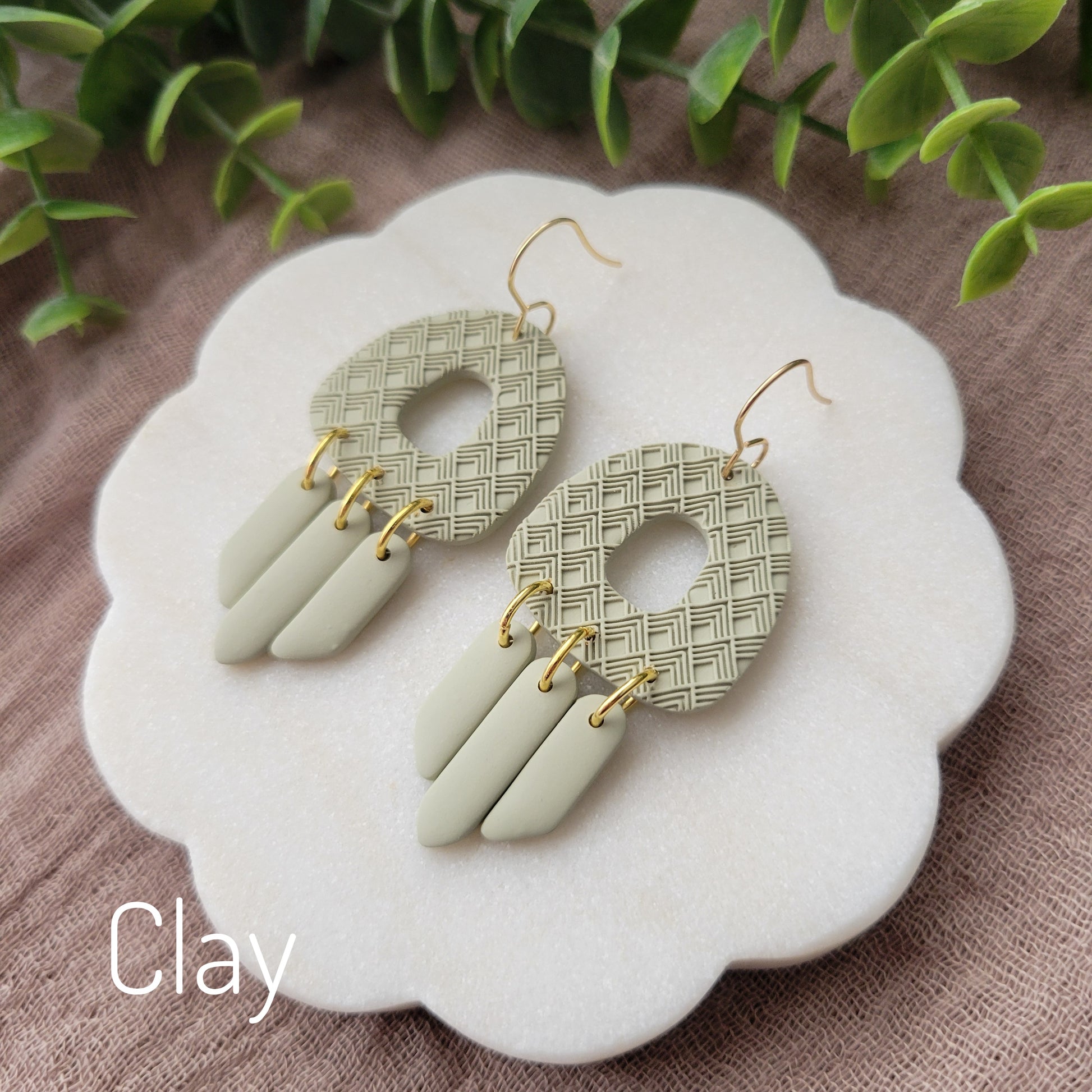 Side view of a pair of green earrings with lattice texture displayed on a white round scalloped tray.