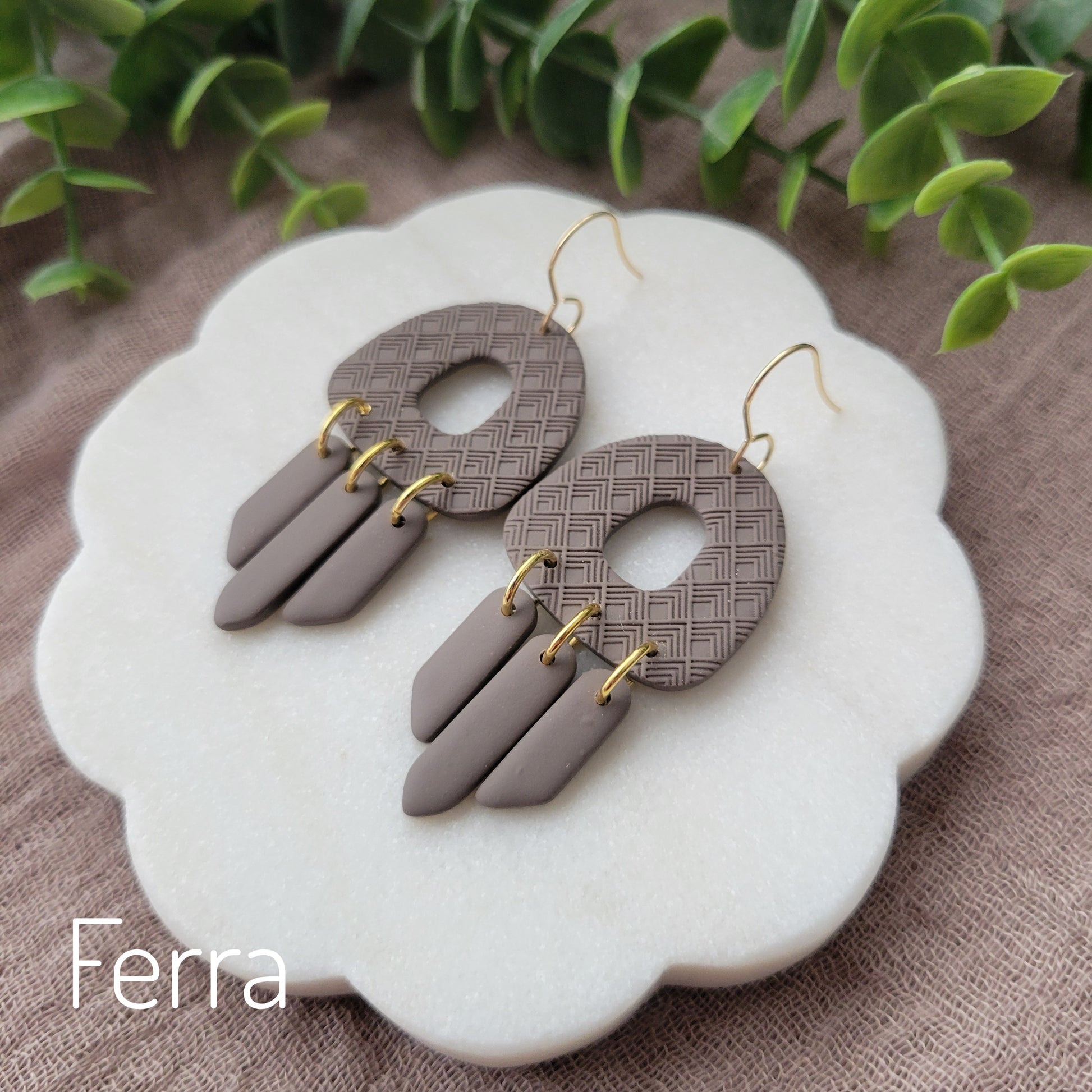 Side view of a pair of dark brown earrings with lattice texture displayed on a white round scalloped tray.