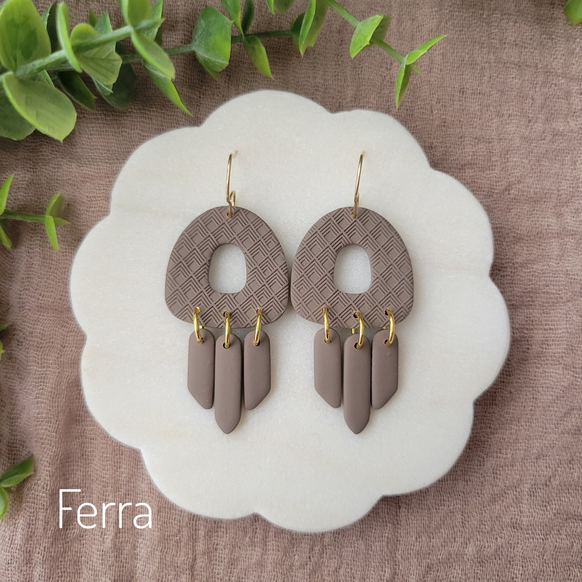 Top view of a pair of dark brown earrings with lattice texture displayed on a white round scalloped tray.