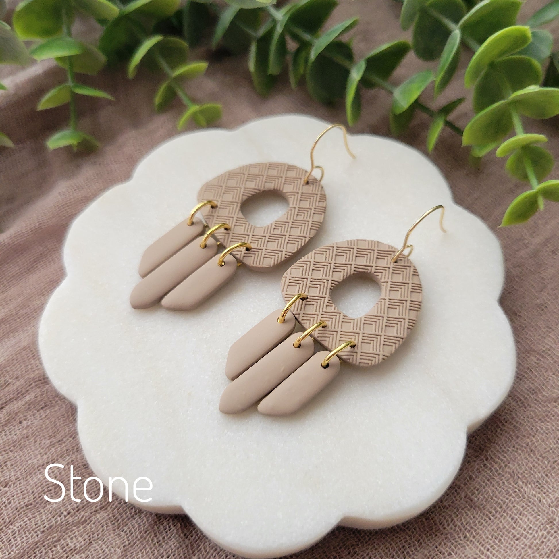 Side view of a pair of light brown earrings with lattice texture displayed on a white round scalloped tray.