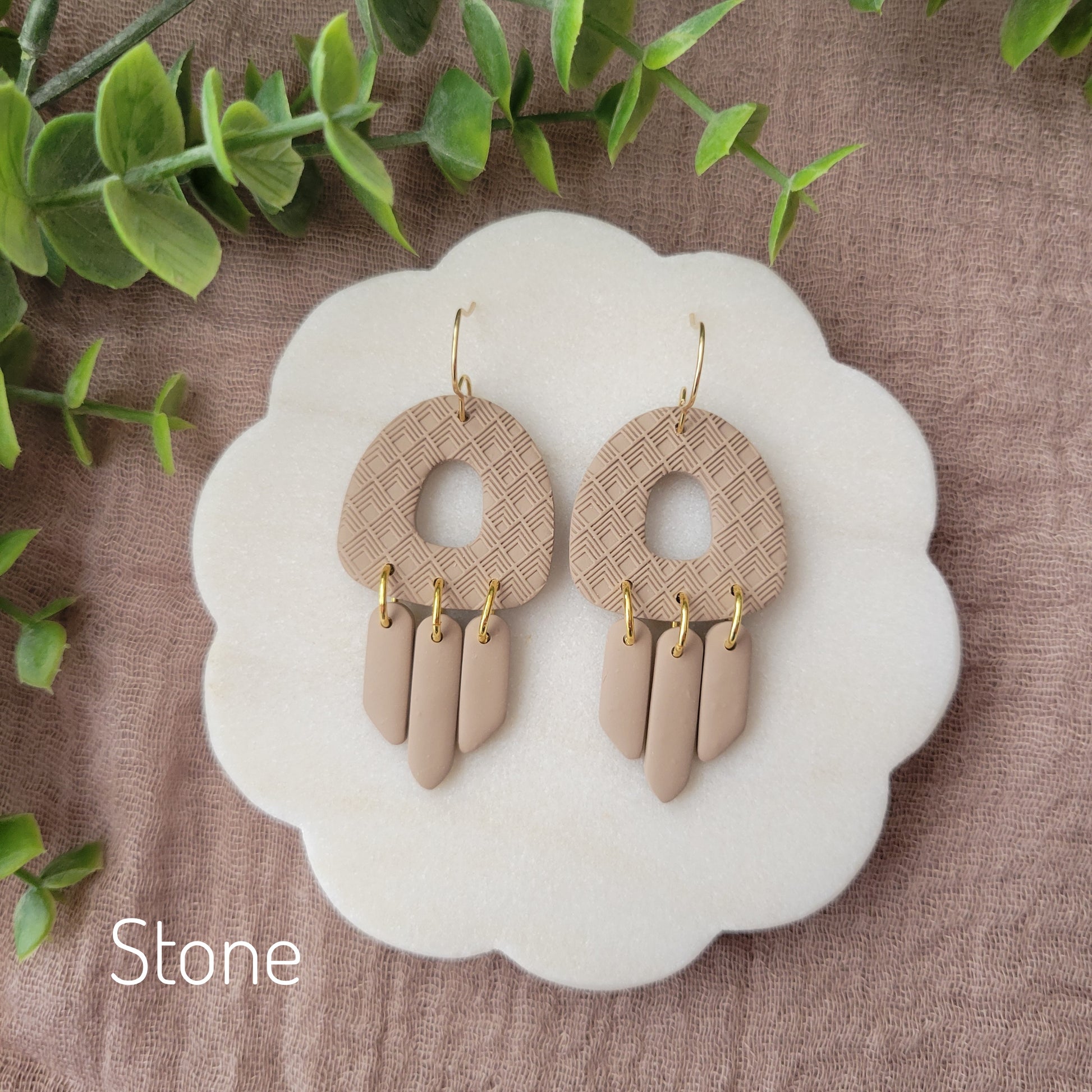 Top view of a pair of light brown earrings with lattice texture displayed on a white round scalloped tray.