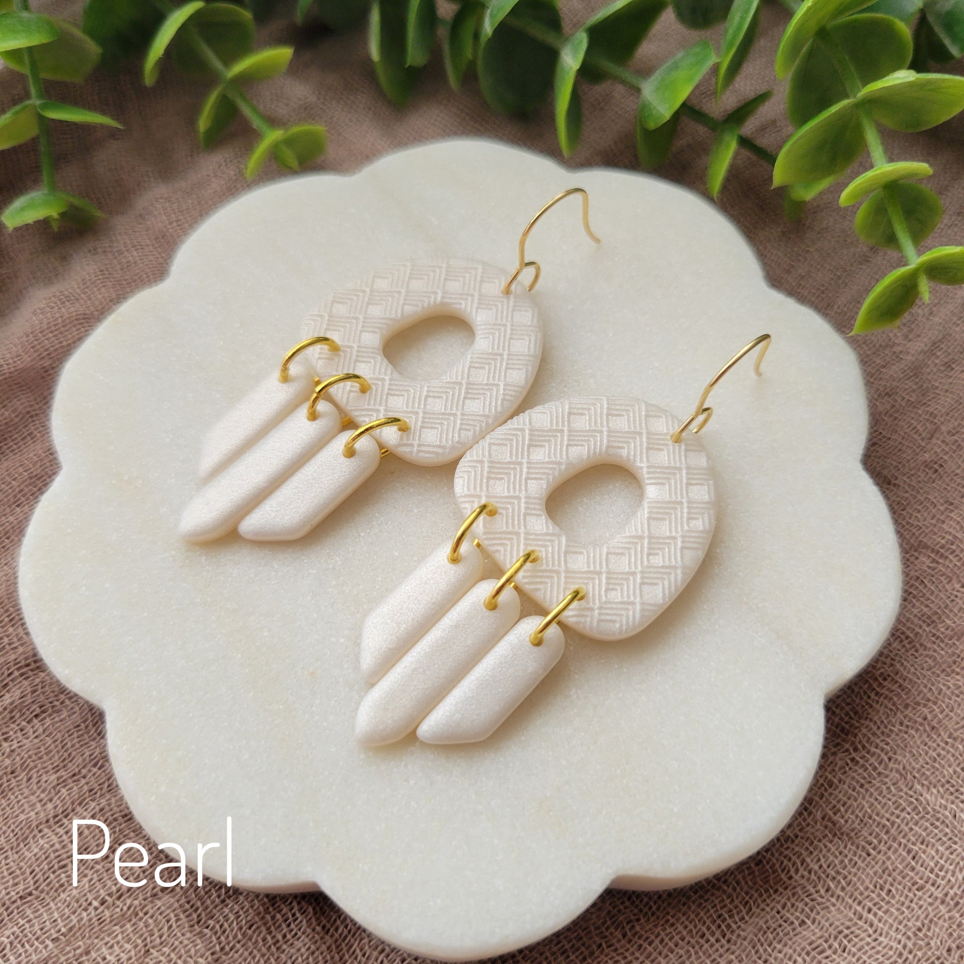 Side view of a pair of pearl earrings with lattice texture displayed on a white round scalloped tray.