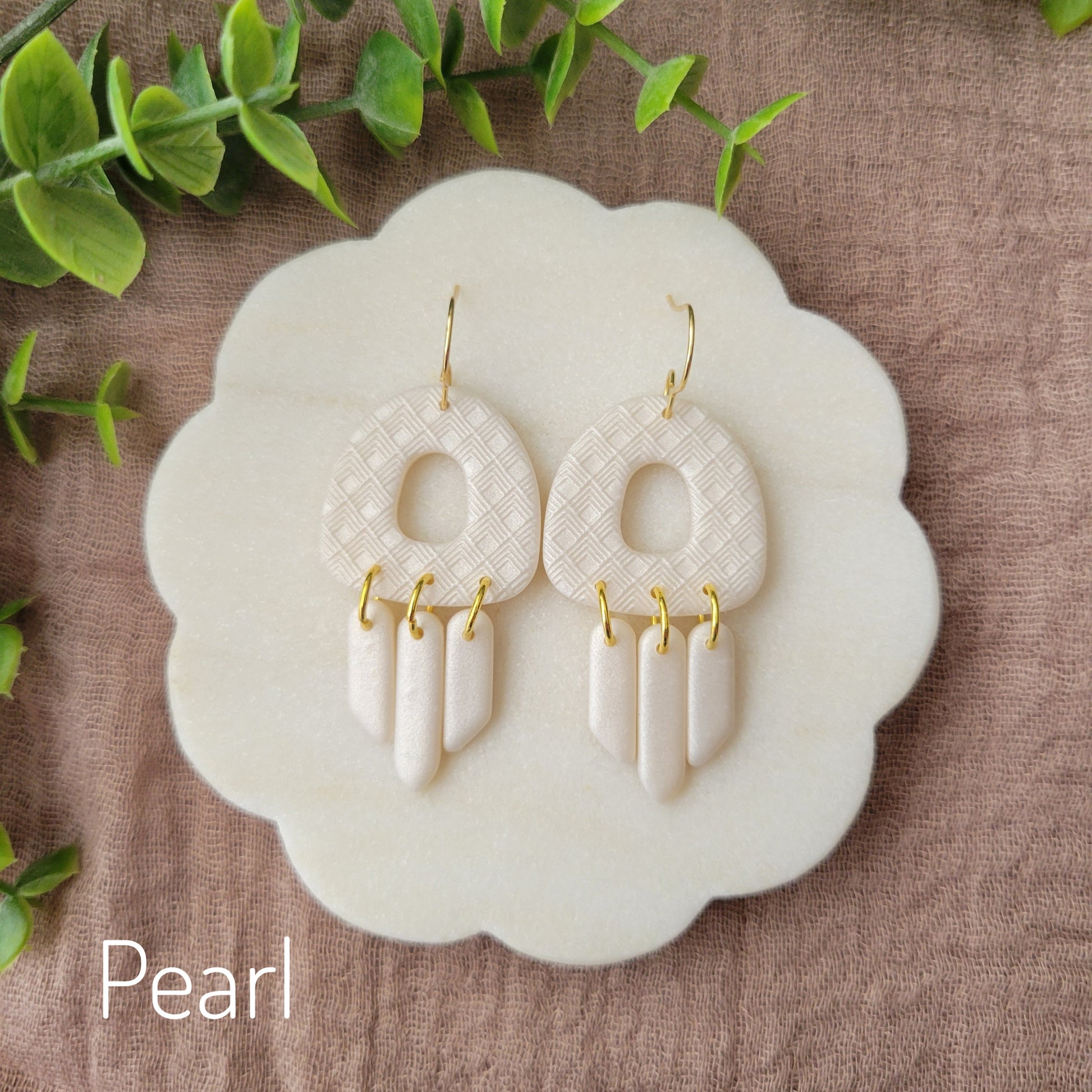 Top view of a pair of pearl earrings with lattice texture displayed on a white round scalloped tray.