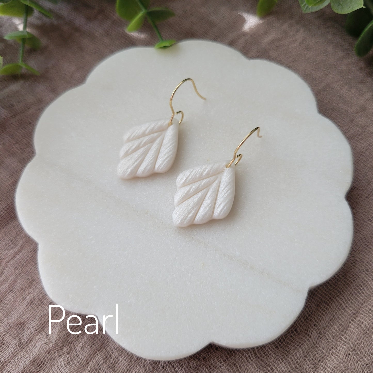 Side view of a pair of small pearl leaf shaped earrings displayed on a white round scalloped tray.