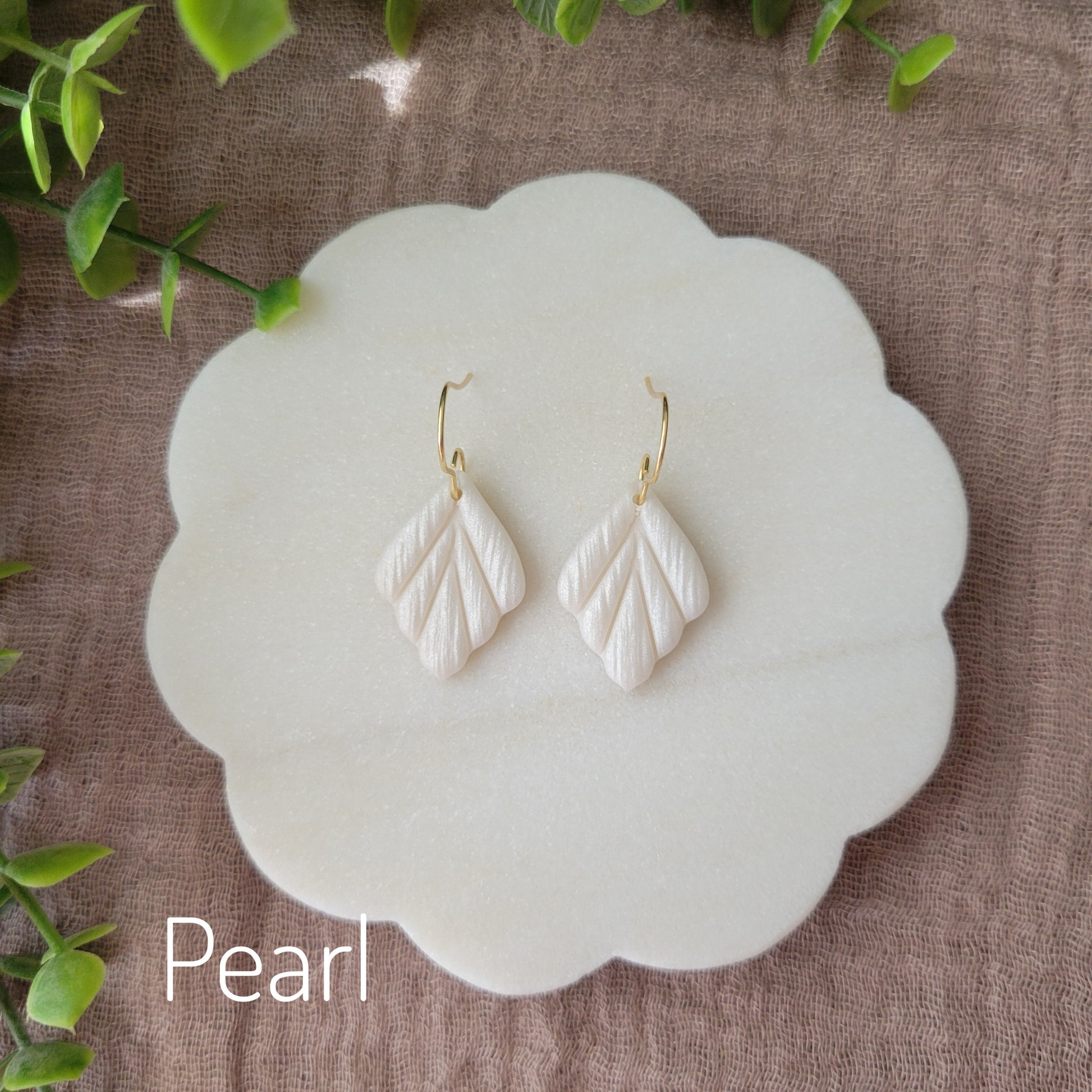 Top view of a pair of small pearl leaf shaped earrings displayed on a white round scalloped tray.