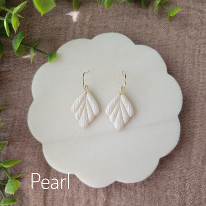 Top view of a pair of small pearl leaf shaped earrings displayed on a white round scalloped tray.