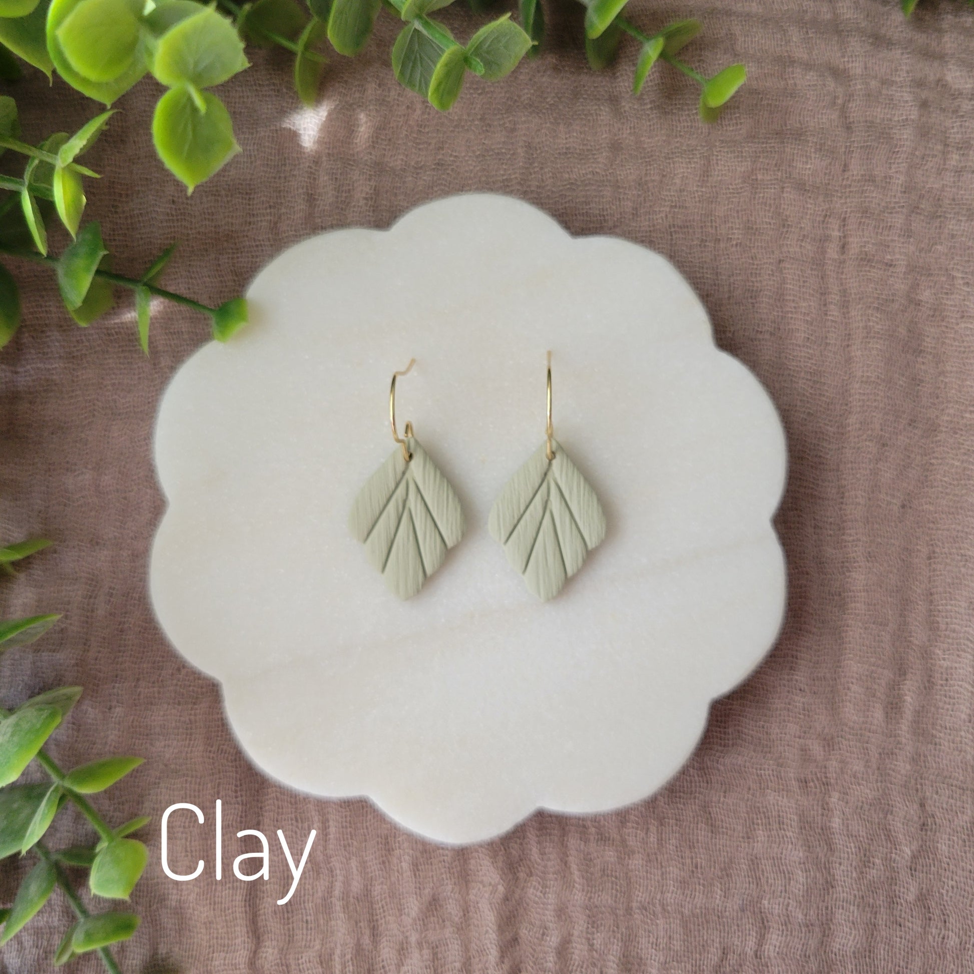 Top view of a pair of small green leaf shaped earrings displayed on a white round scalloped tray.