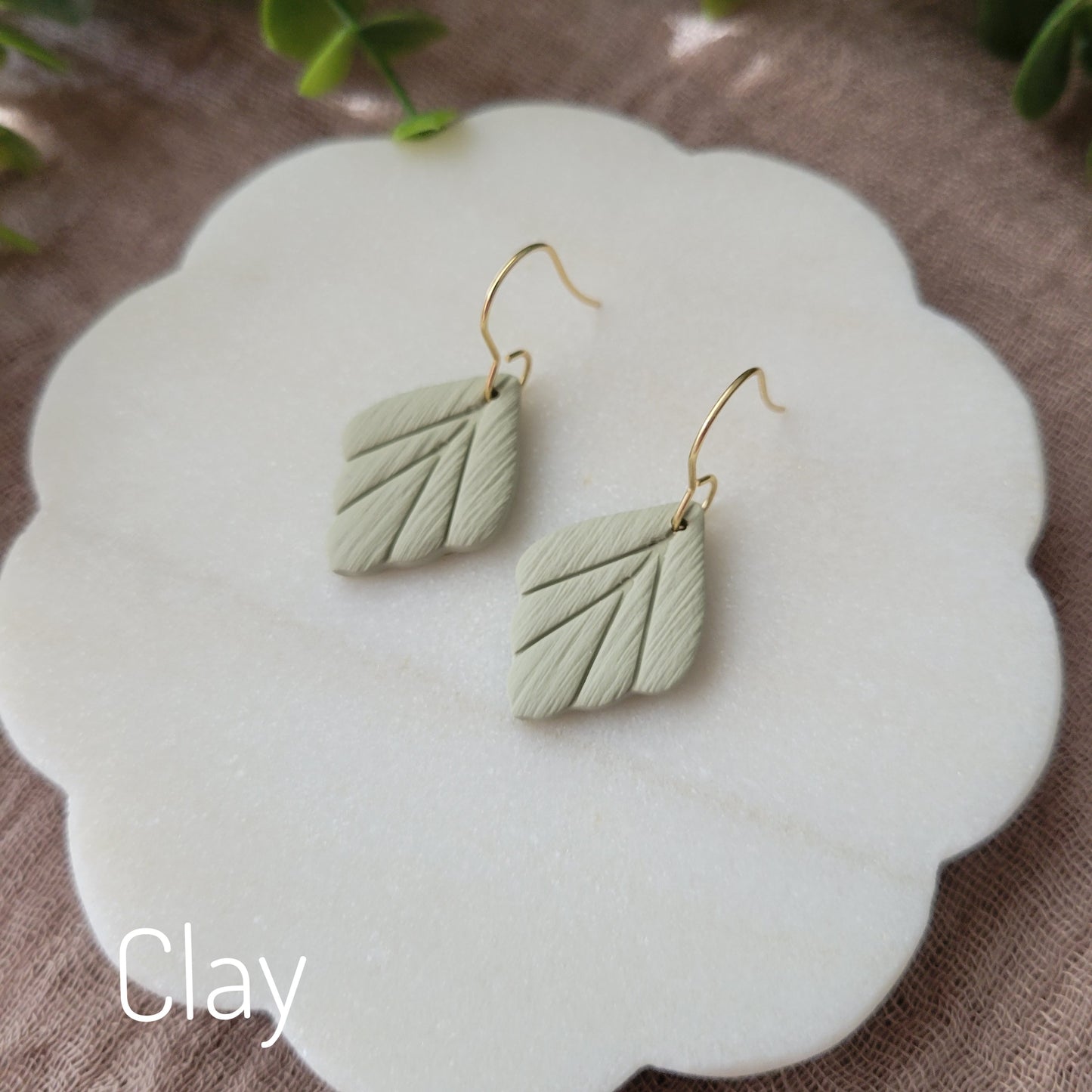 Side view of a pair of small green leaf shaped earrings displayed on a white round scalloped tray.