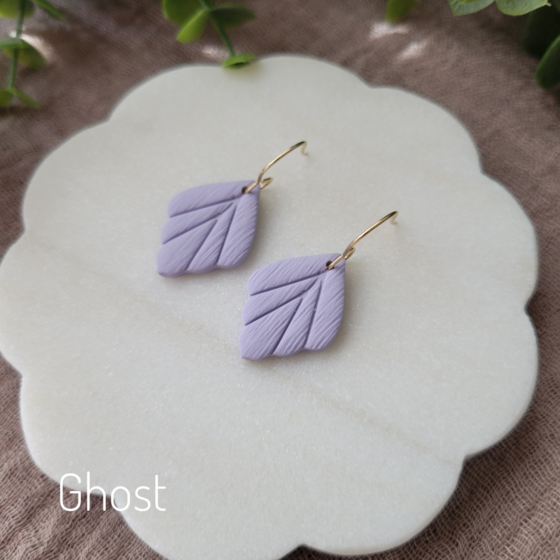 Side view of a pair of small purple leaf shaped earrings displayed on a white round scalloped tray.