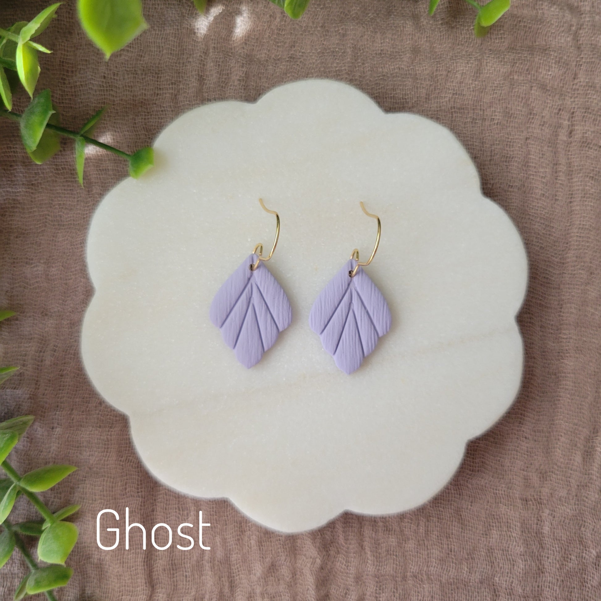 Top view of a pair of small purple leaf shaped earrings displayed on a white round scalloped tray.