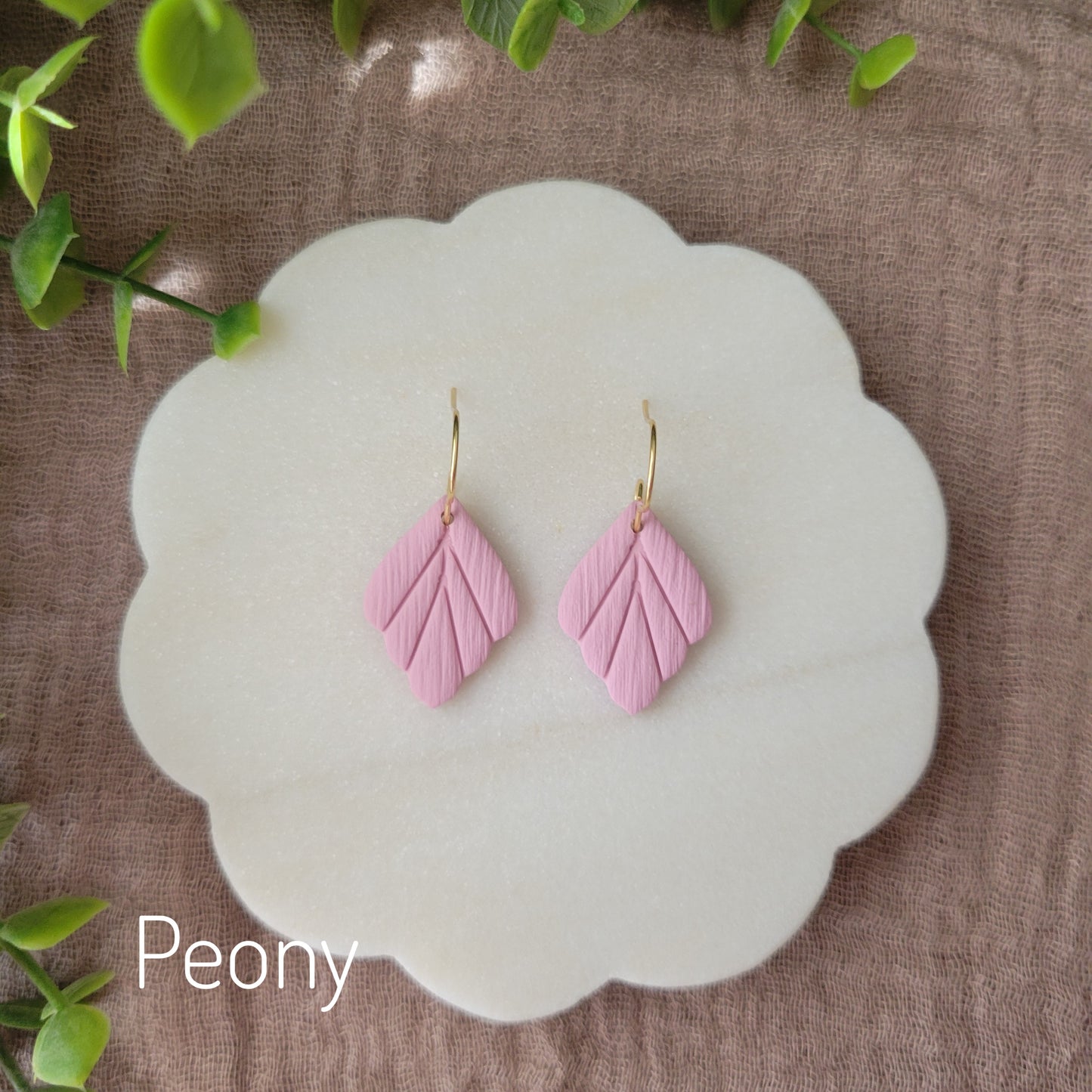 Top view of a pair of small pink leaf shaped earrings displayed on a white round scalloped tray.