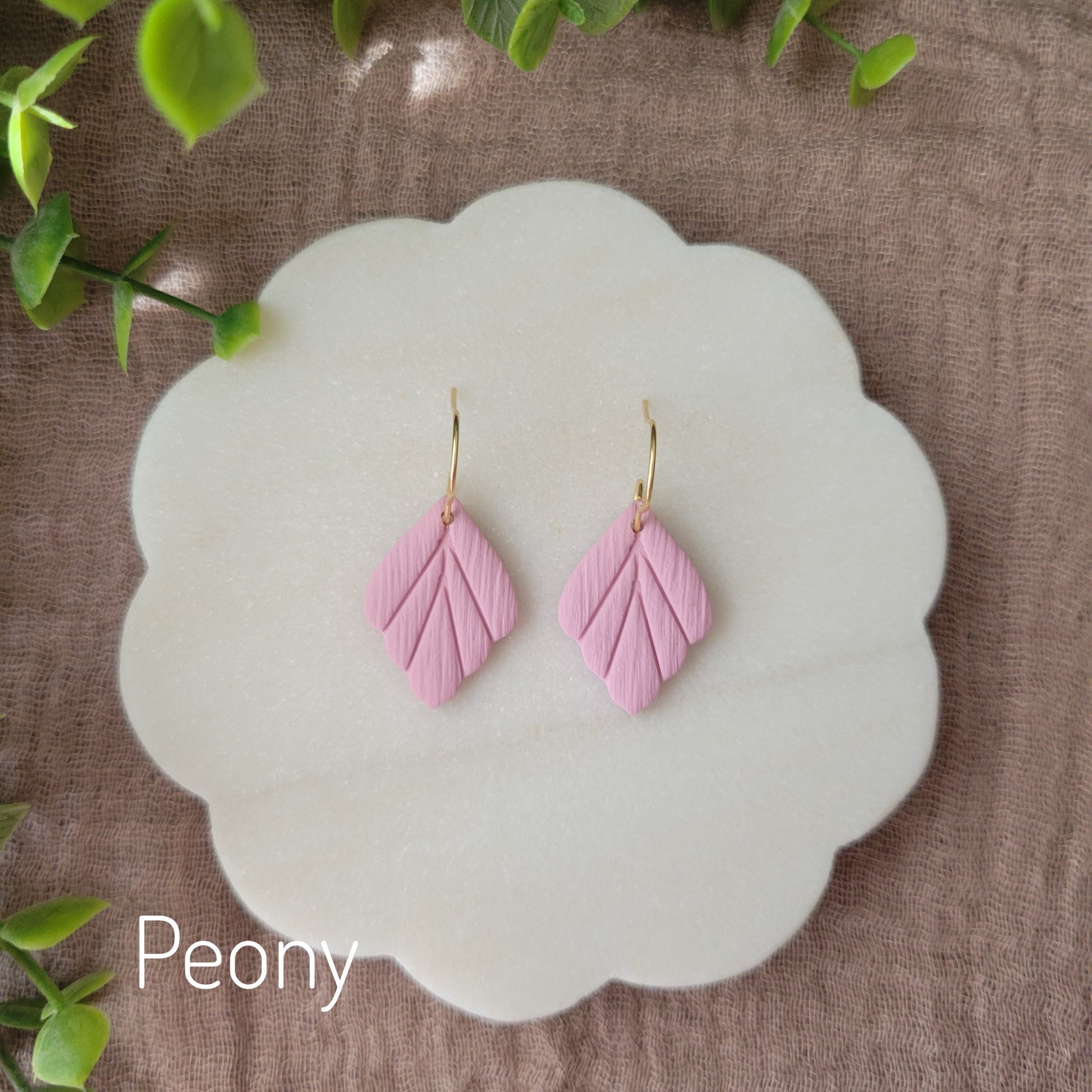 Top view of a pair of small pink leaf shaped earrings displayed on a white round scalloped tray.