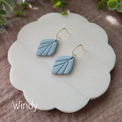 Side view of a pair of small blue leaf shaped earrings displayed on a white round scalloped tray.