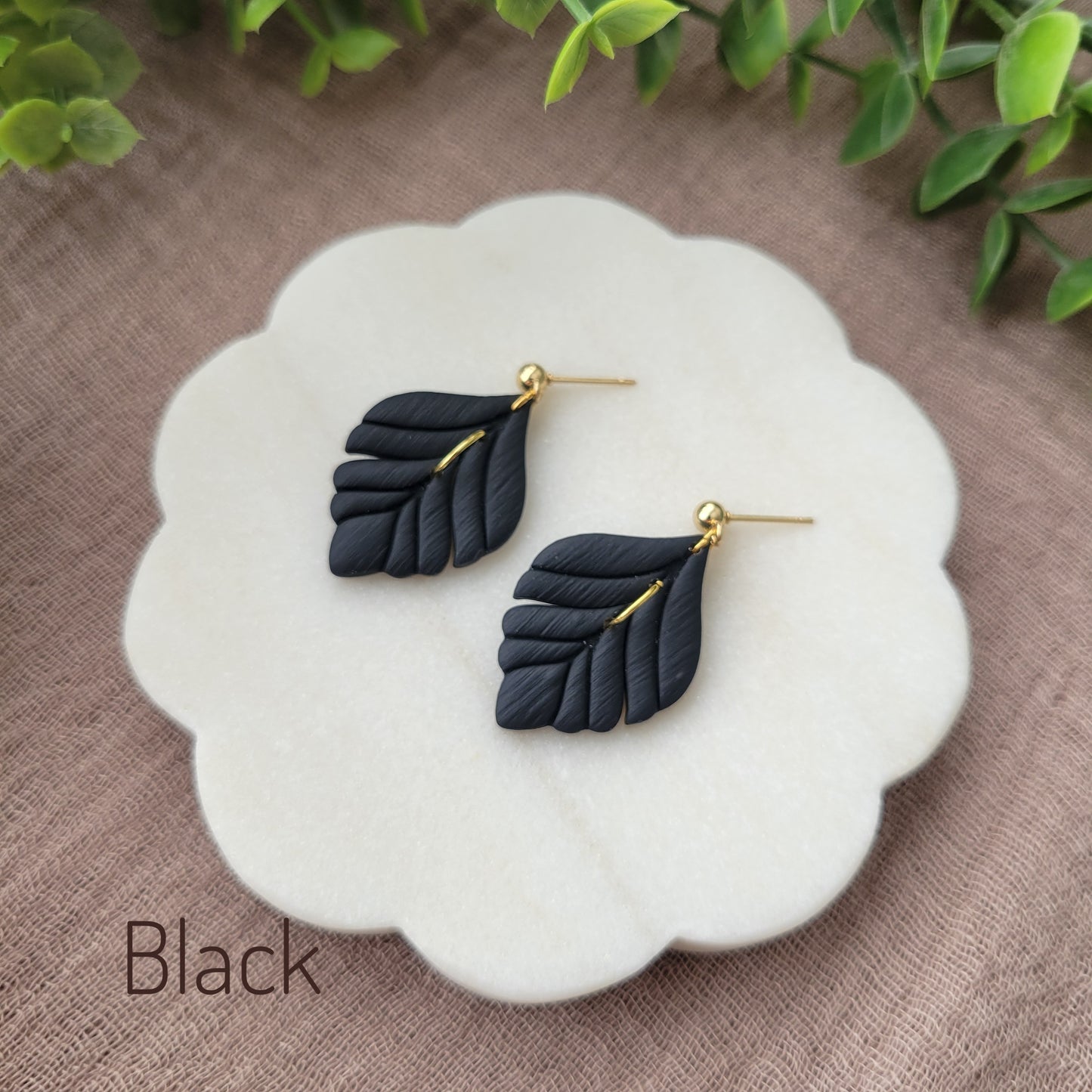 Side view of a pair of black elegant leaf shaped earrings displayed o a a white round scalloped tray.