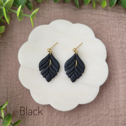 Top view of a pair of black elegant leaf shaped earrings displayed on a white round scalloped tray.