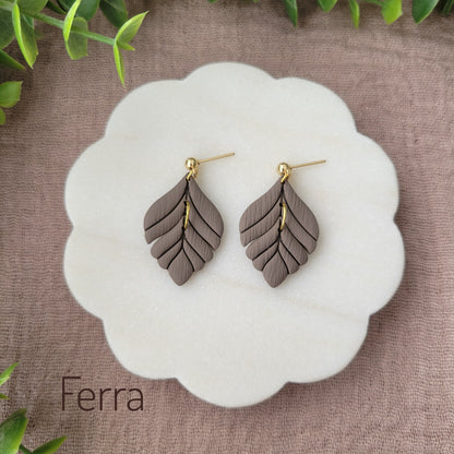 Top view of a pair of greyish brown elegant leaf shaped earrings displayed on a white round scalloped tray.