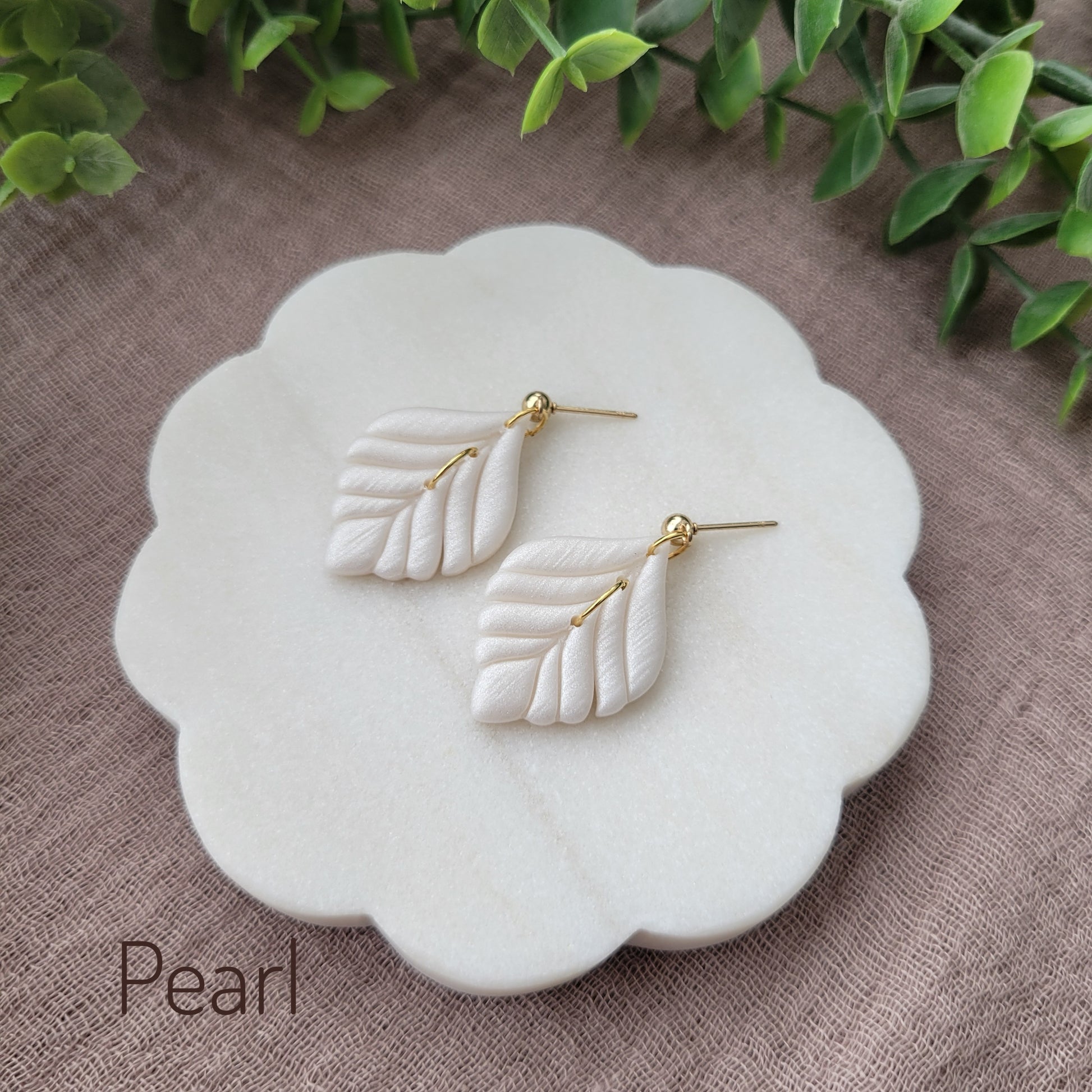 Side view of a pair of pearl elegant leaf shaped earrings displayed on a white round scalloped tray.