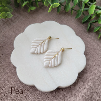 Side view of a pair of pearl elegant leaf shaped earrings displayed on a white round scalloped tray.