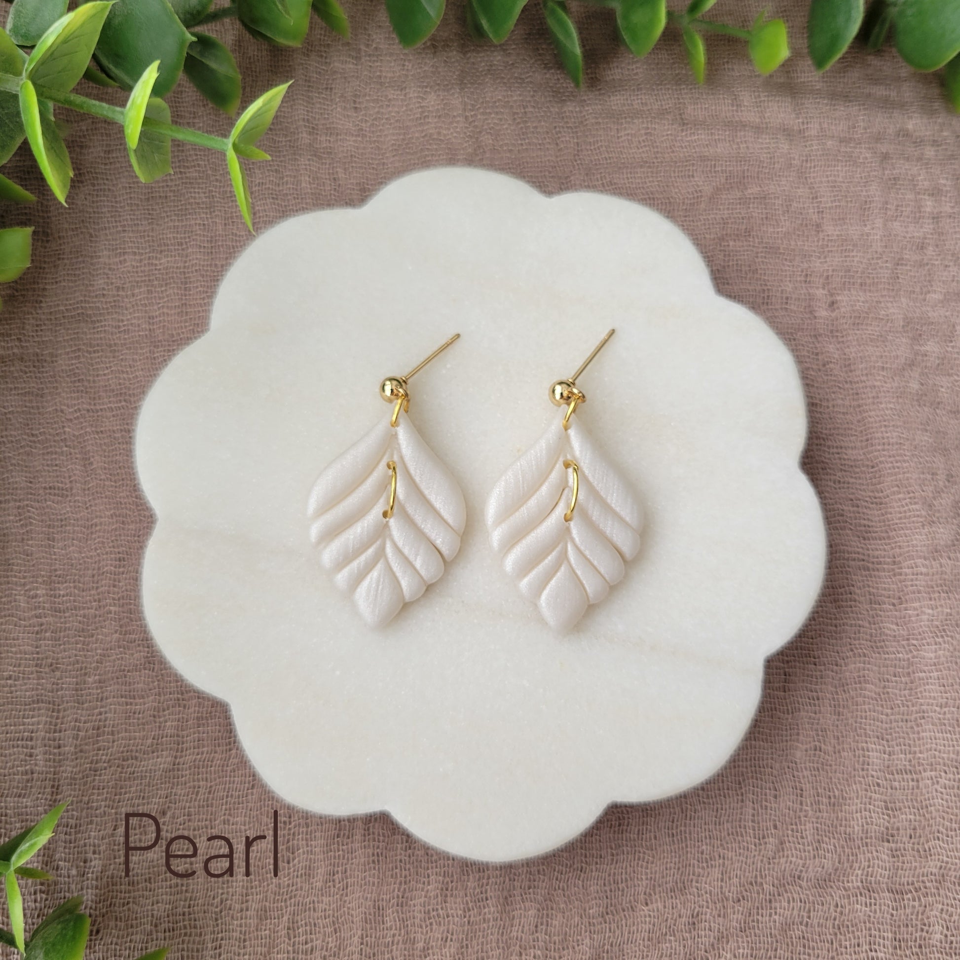 Top view of a pair of pearl elegant leaf shaped earrings displayed on a white round scalloped tray.