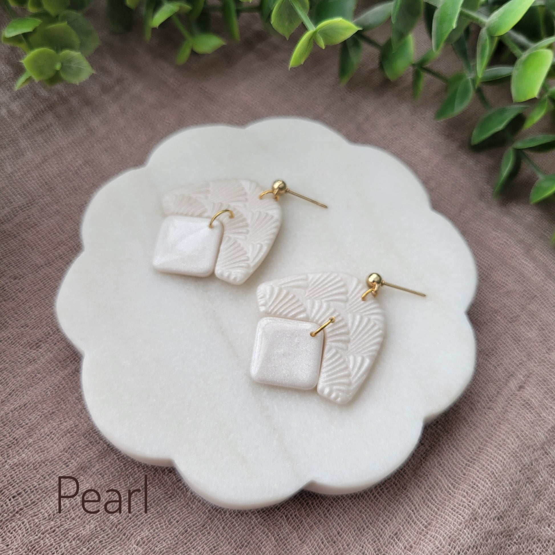 Side view of a pair of pearl colored earrings with a scalloped texture displayed on a white scalloped tray.