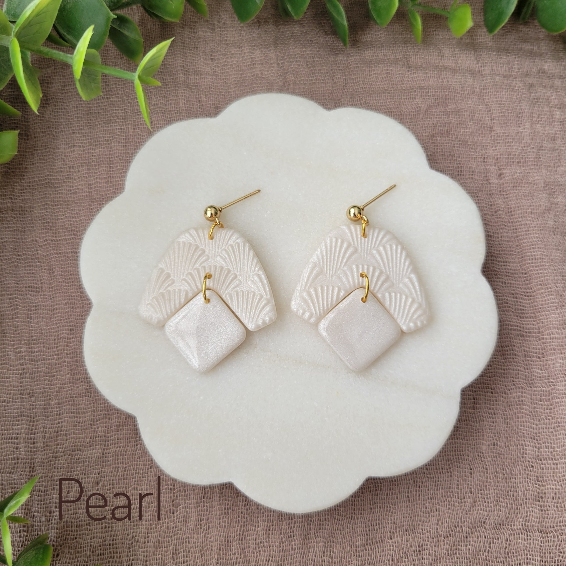 Top view of a pair of pearl colored earrings with a scalloped texture displayed on a white scalloped tray.