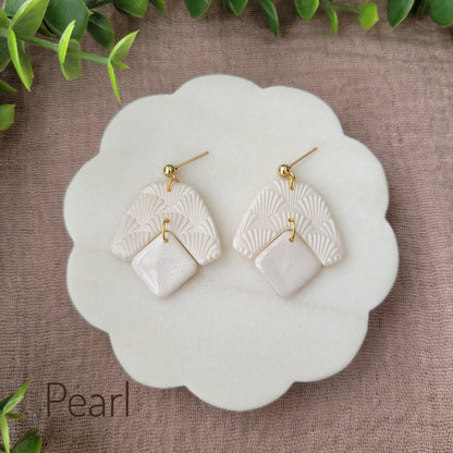 Top view of a pair of pearl colored earrings with a scalloped texture displayed on a white scalloped tray.