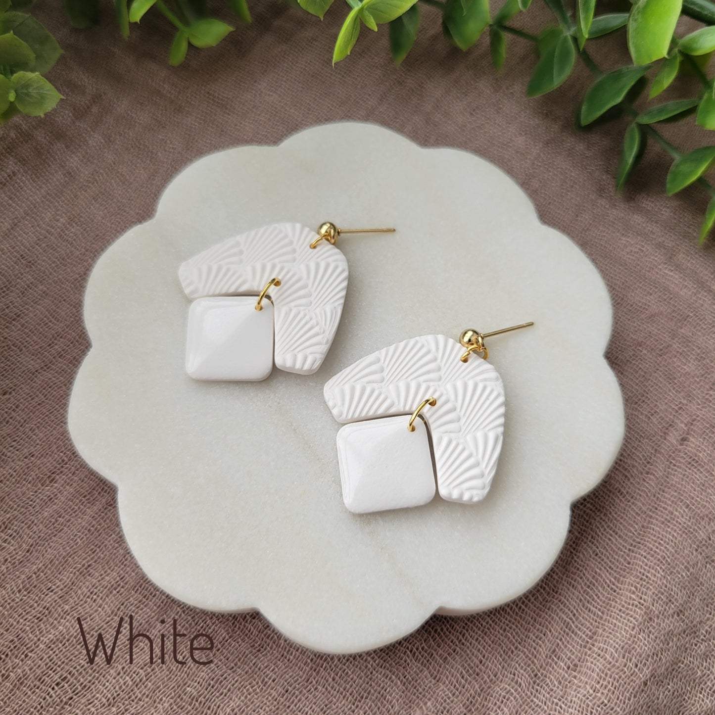 Side view of a pair of white colored earrings with a scalloped texture displayed on a white scalloped tray.