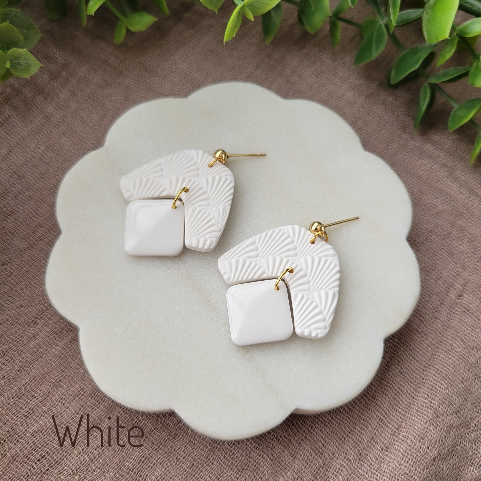 Side view of a pair of white colored earrings with a scalloped texture displayed on a white scalloped tray.