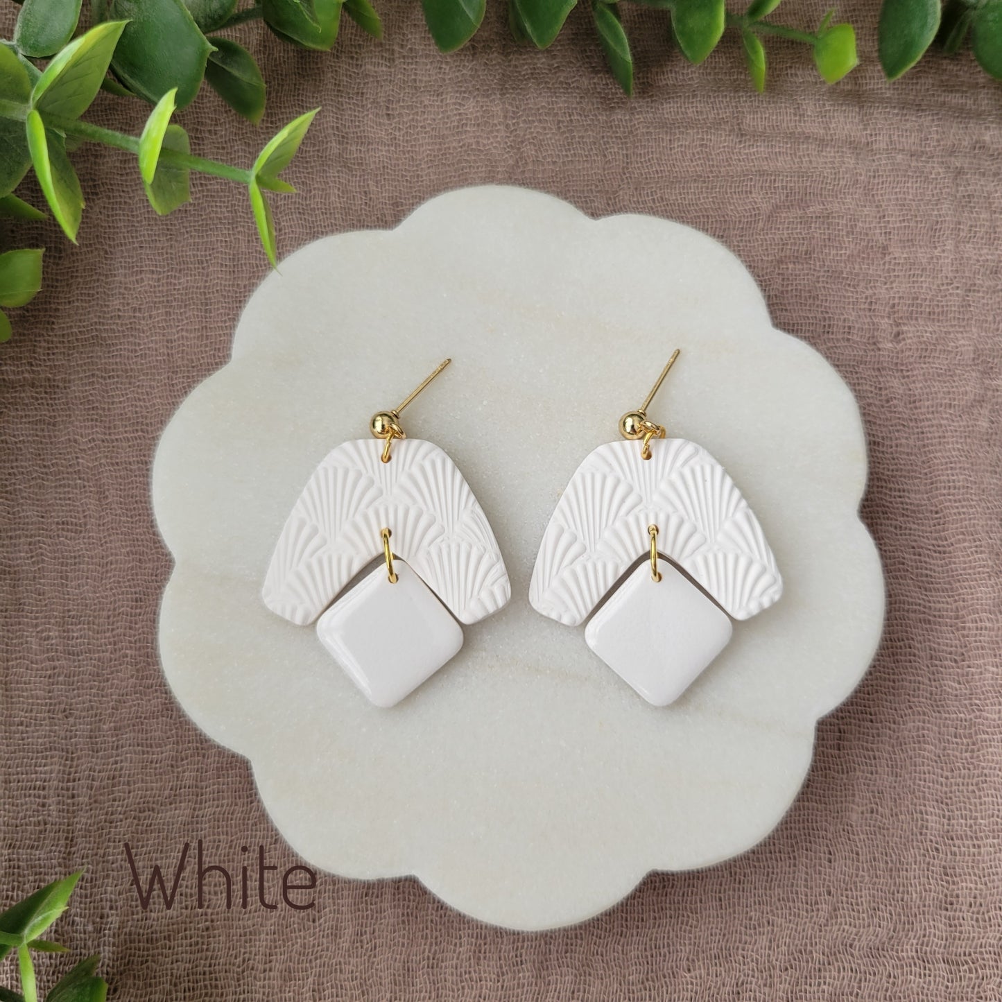 Top view of a pair of white colored earrings with a scalloped texture displayed on a white scalloped tray.