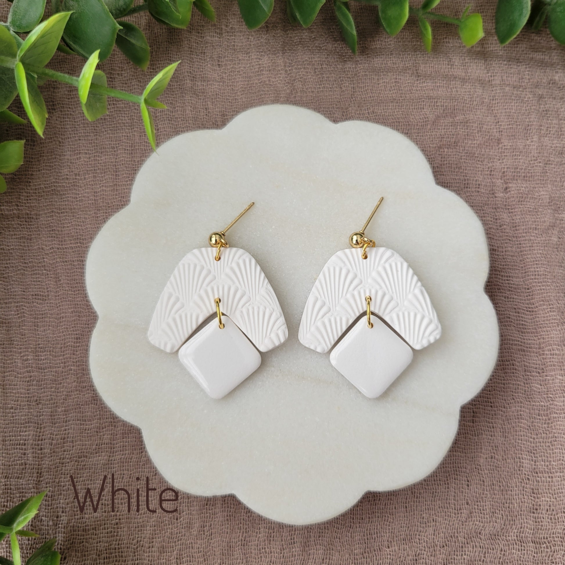 Top view of a pair of white colored earrings with a scalloped texture displayed on a white scalloped tray.