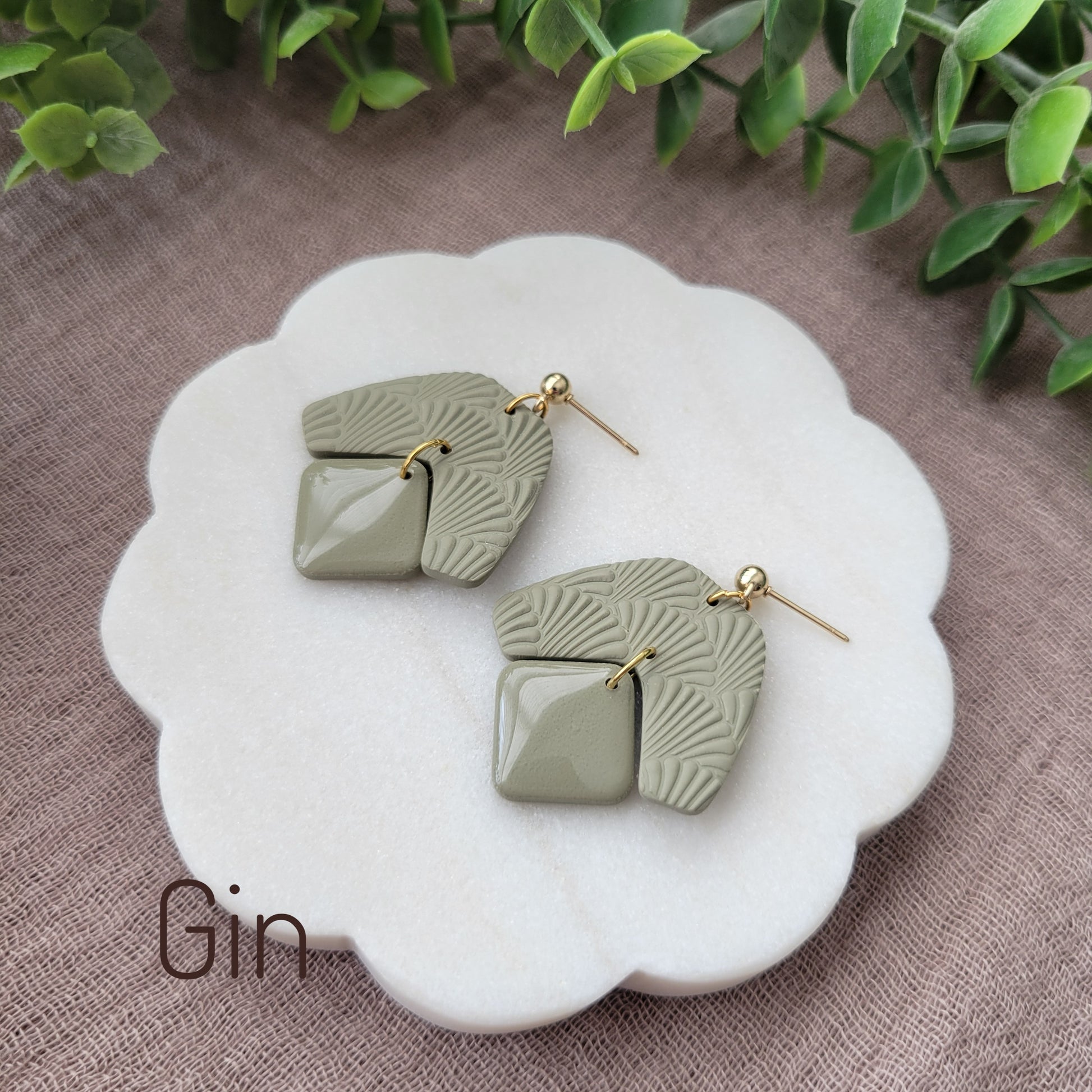 Side view of a pair of light green colored earrings with a scalloped texture displayed on a white scalloped tray.