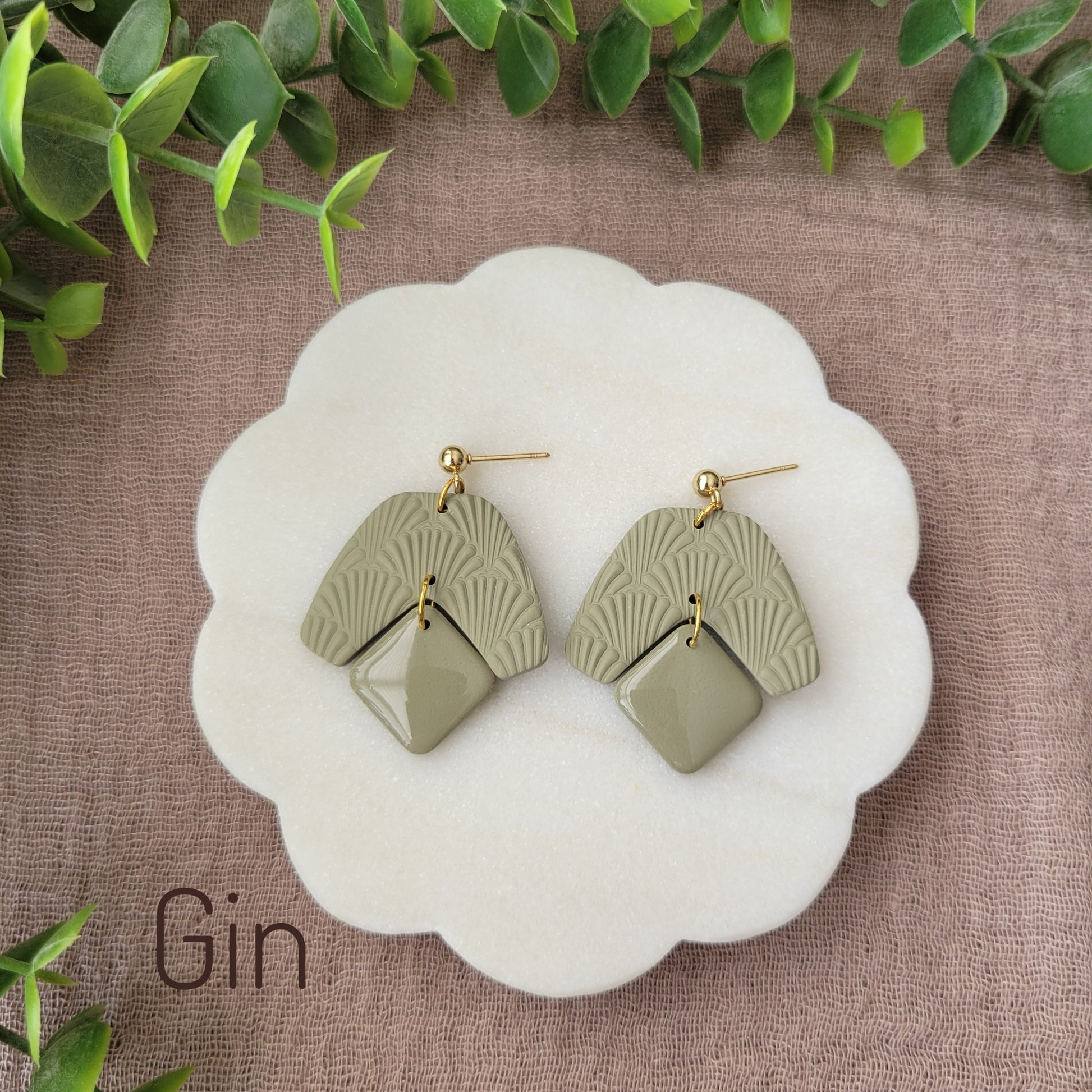 Top view of a pair of light green colored earrings with a scalloped texture displayed on a white scalloped tray.