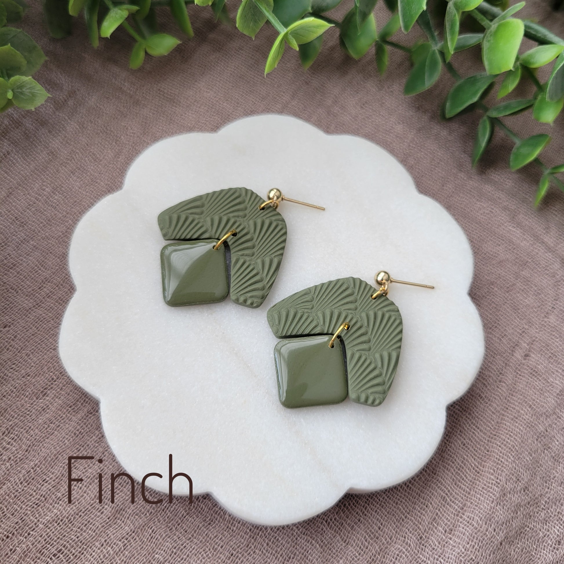 Side view of a pair of dark green colored earrings with a scalloped texture displayed on a white scalloped tray.