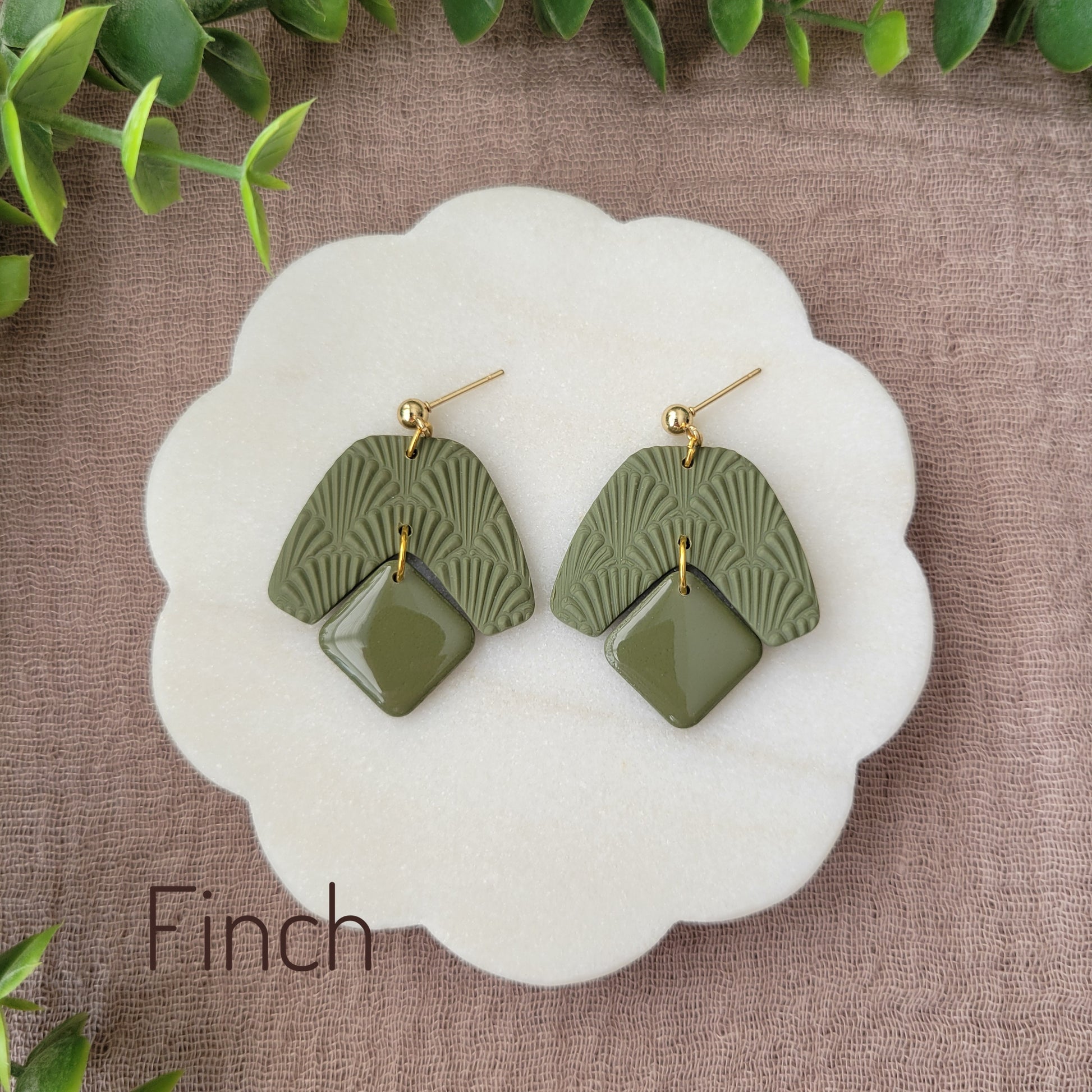 Top view of a pair of dark green colored earrings with a scalloped texture displayed on a white scalloped tray.
