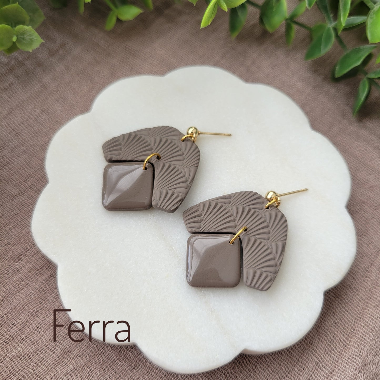 Side view of a pair of dark brown colored earrings with a scalloped texture displayed on a white scalloped tray.