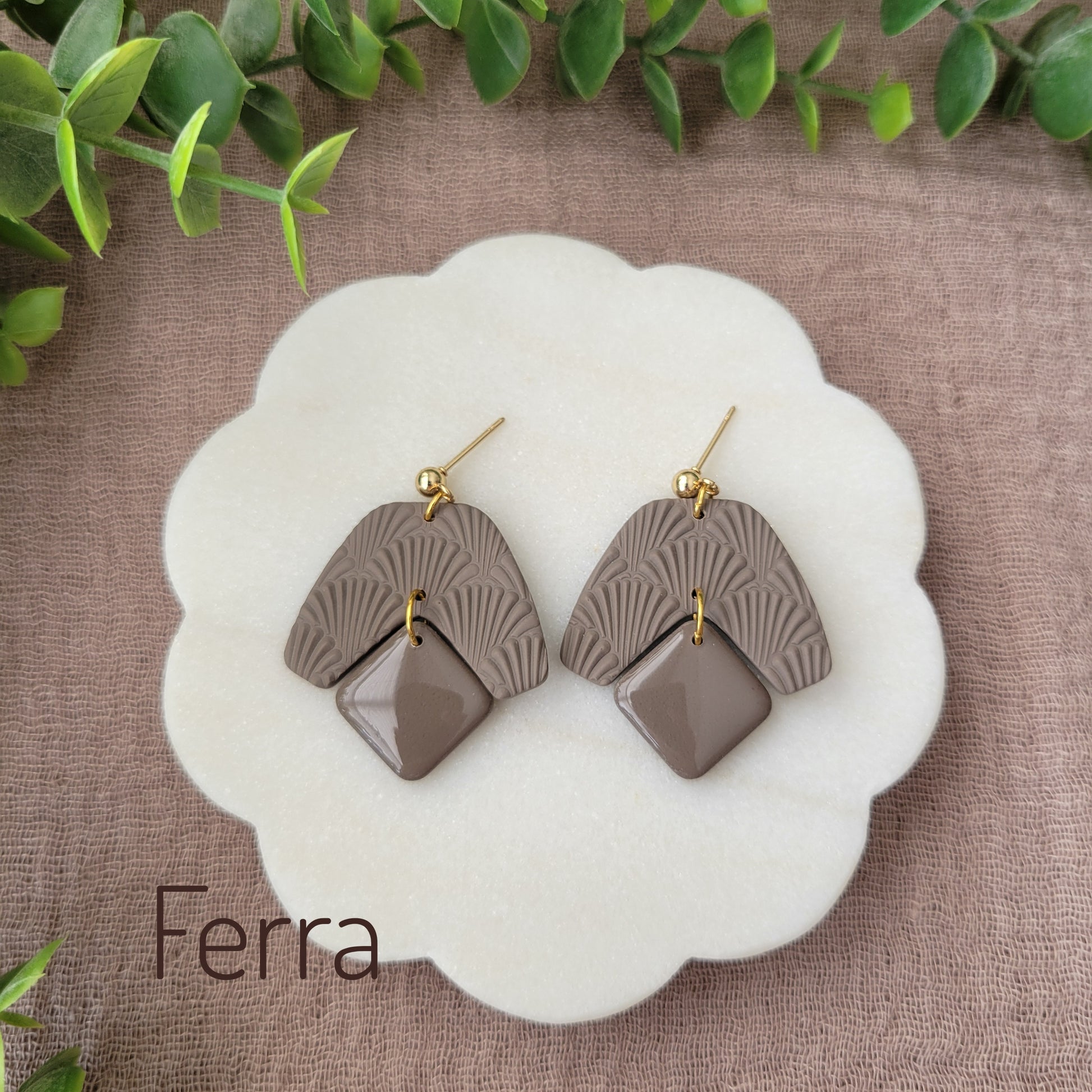 Top view of a pair of dark brown colored earrings with a scalloped texture displayed on a white scalloped tray.