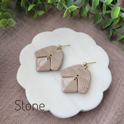 Side view of a pair of light brown colored earrings with a scalloped texture displayed on a white scalloped tray.