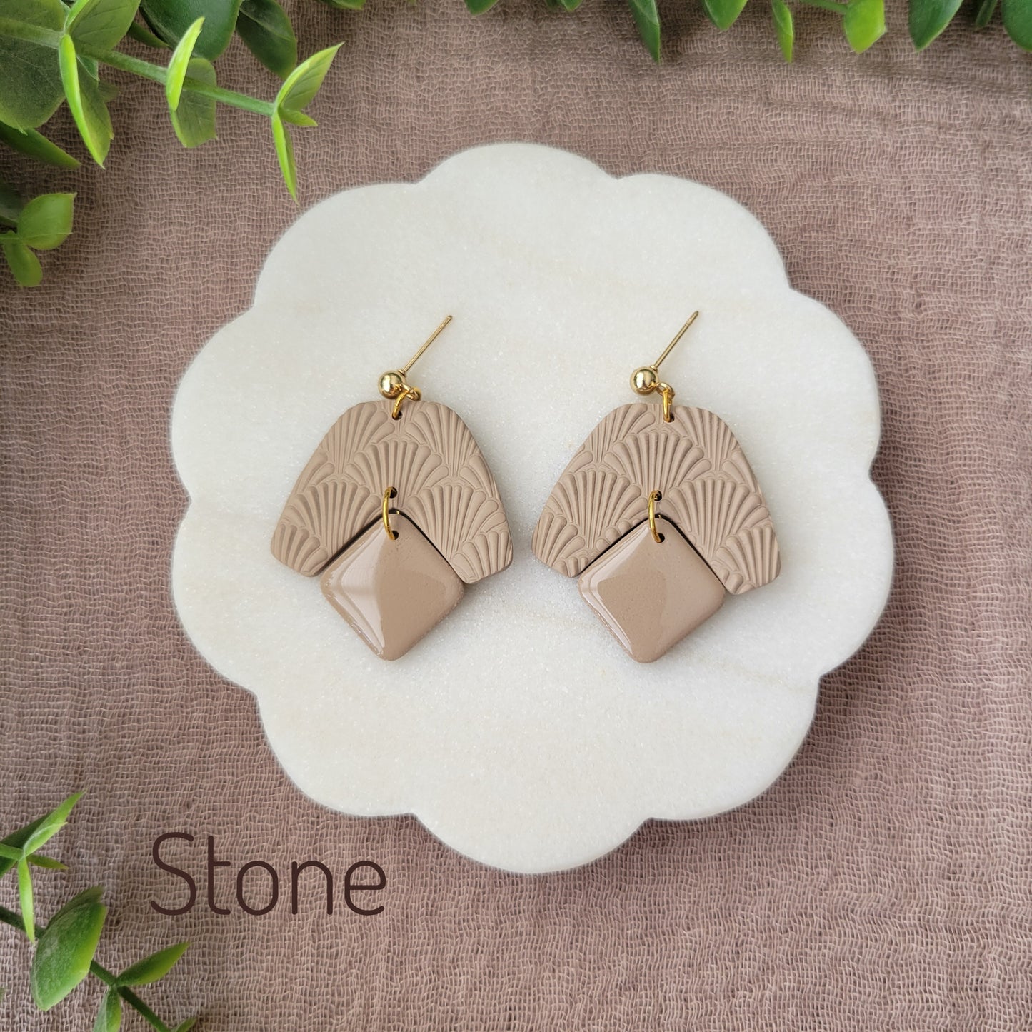 Top view of a pair of light brown colored earrings with a scalloped texture displayed on a white scalloped tray.