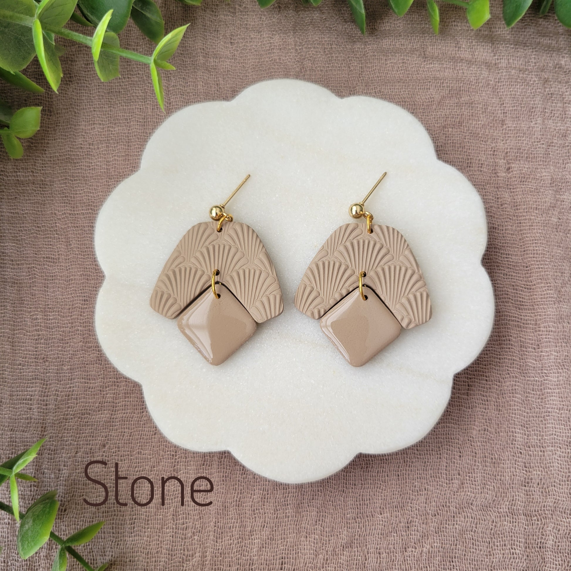 Top view of a pair of light brown colored earrings with a scalloped texture displayed on a white scalloped tray.