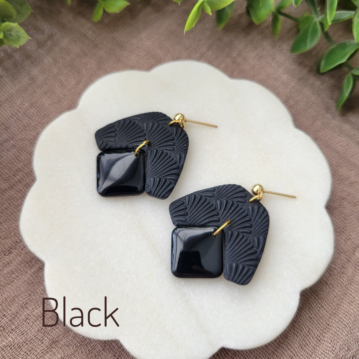 Side view of a pair of black colored earrings with a scalloped texture displayed on a white scalloped tray.