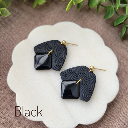 Side view of a pair of black colored earrings with a scalloped texture displayed on a white scalloped tray.