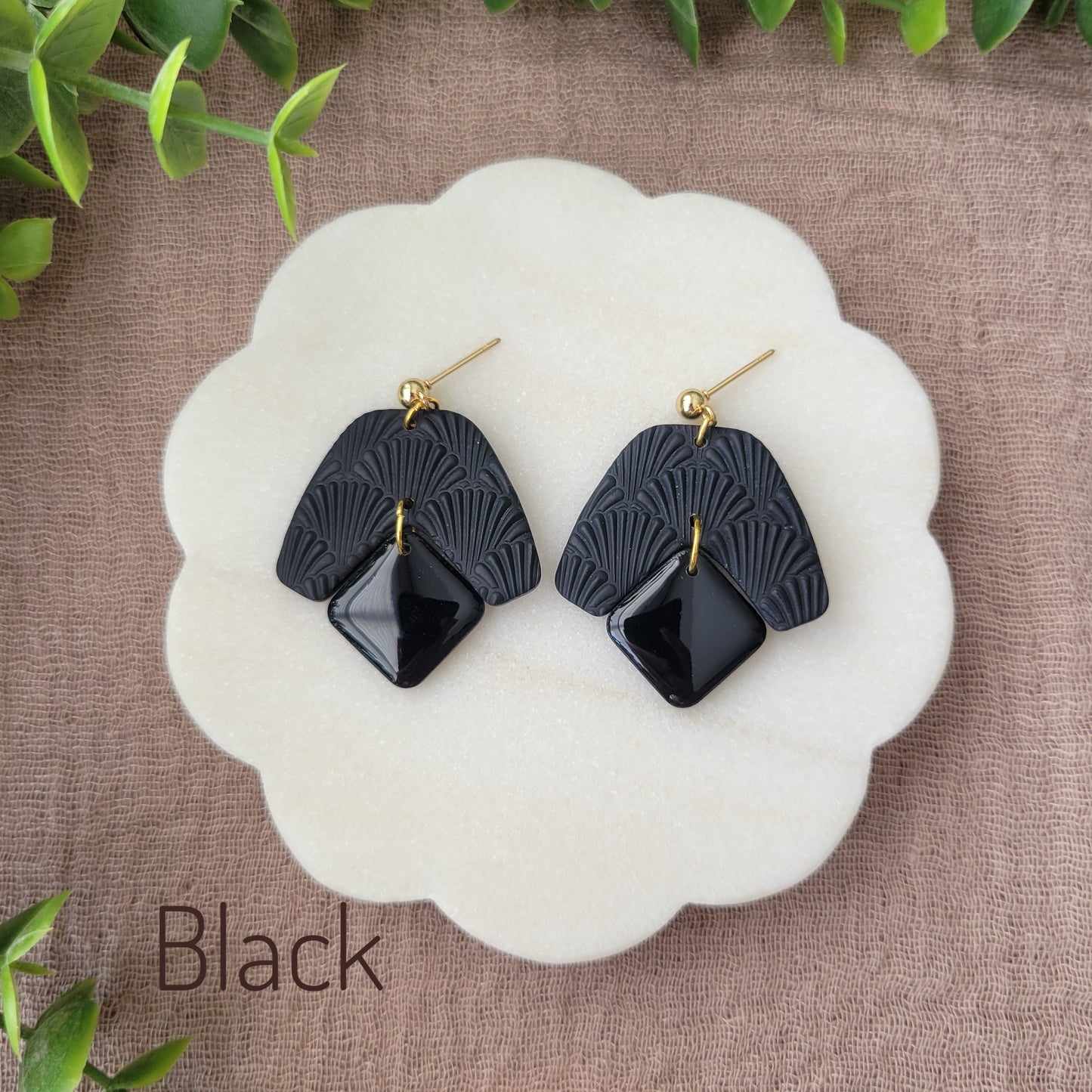 Top view of a pair of black colored earrings with a scalloped texture displayed on a white scalloped tray.