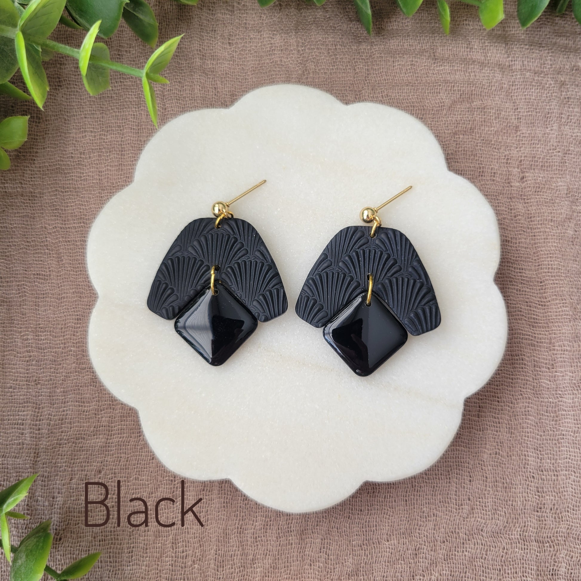 Top view of a pair of black colored earrings with a scalloped texture displayed on a white scalloped tray.