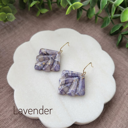 Side view of a pair of lavender marbled earrings displayed on a white round scalloped tray.