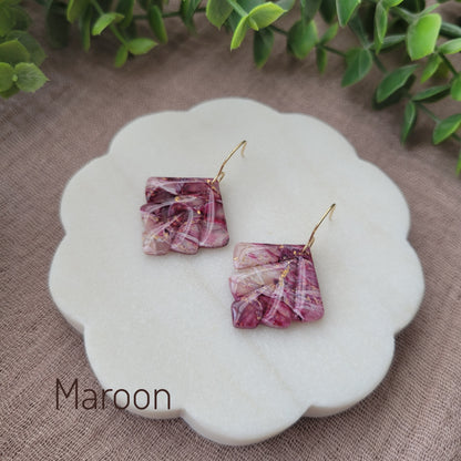 Side view of a pair of maroon marbled earrings displayed on a white round scalloped tray.